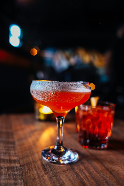 Transparent goblet of red alcoholic drink placed on wooden table near decorated glasses of cocktails in cafeteria on blurred background