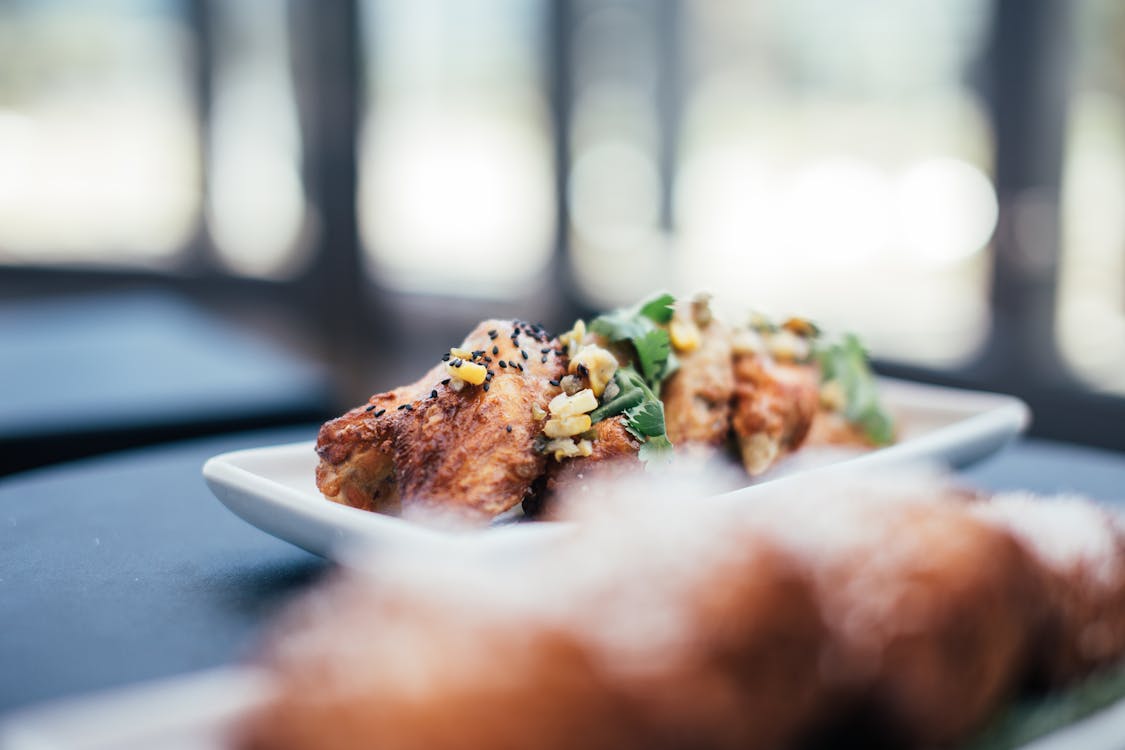 Appetizing roasted chicken wings decorated with parsley and corn served on white plate on table in restaurant on blurred background