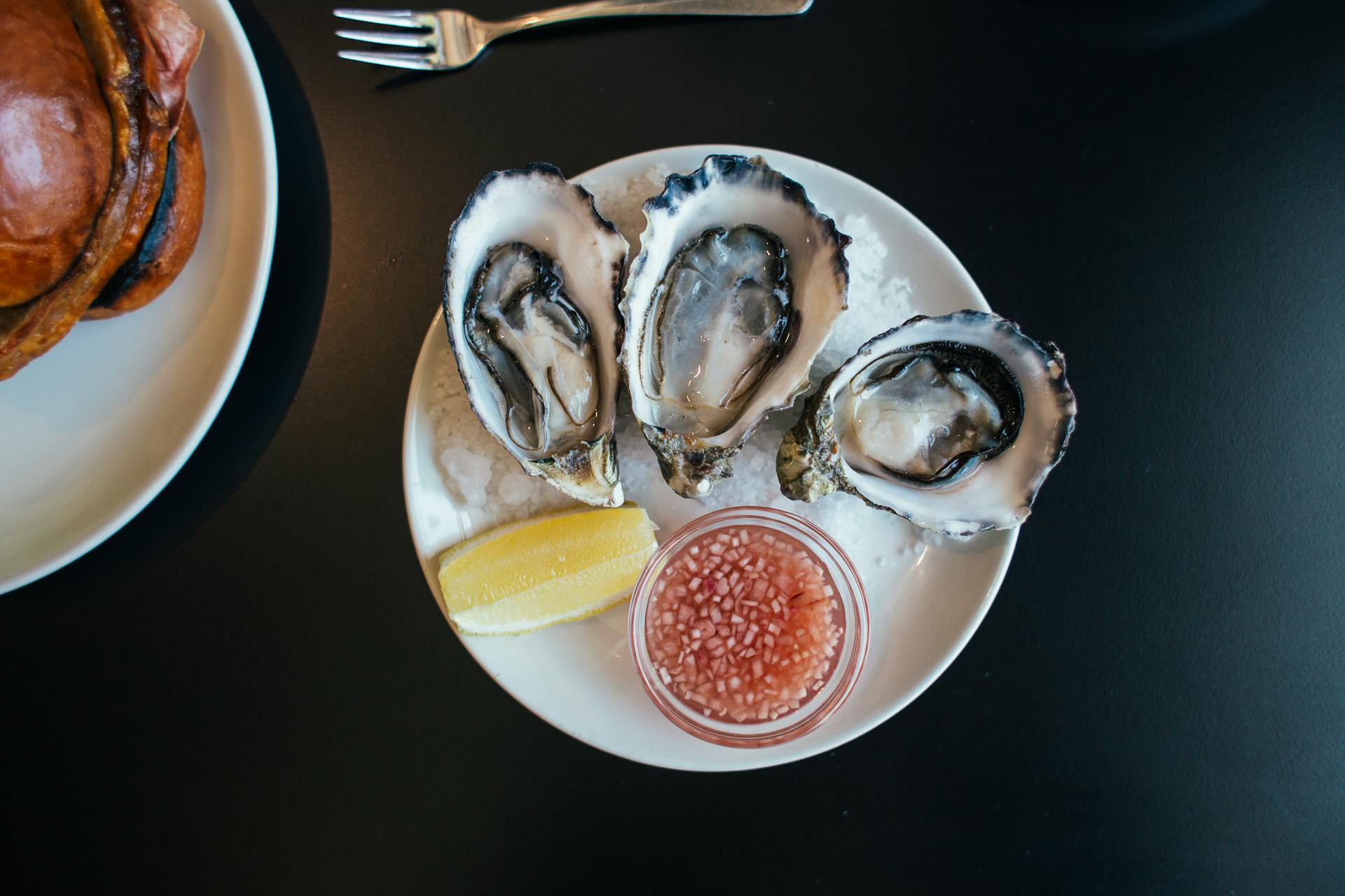 Top view of sophisticated seafood dish with oysters served on plate with sauce and lemon on table in modern restaurant