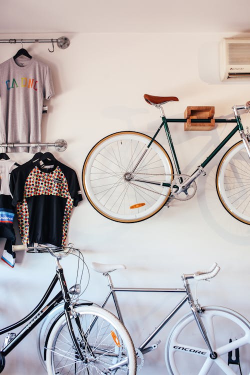 Free Bicycles at white wall with various t shirts hanging on hangers on metal racks in light room with transport in storage Stock Photo