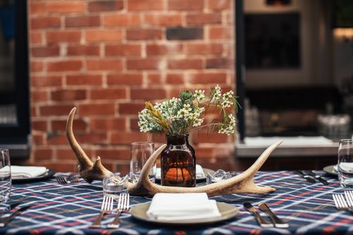Free Glass vase with small white flowers placed on table with plate and cutlery with napkins on terrace of cafe against brick wall Stock Photo