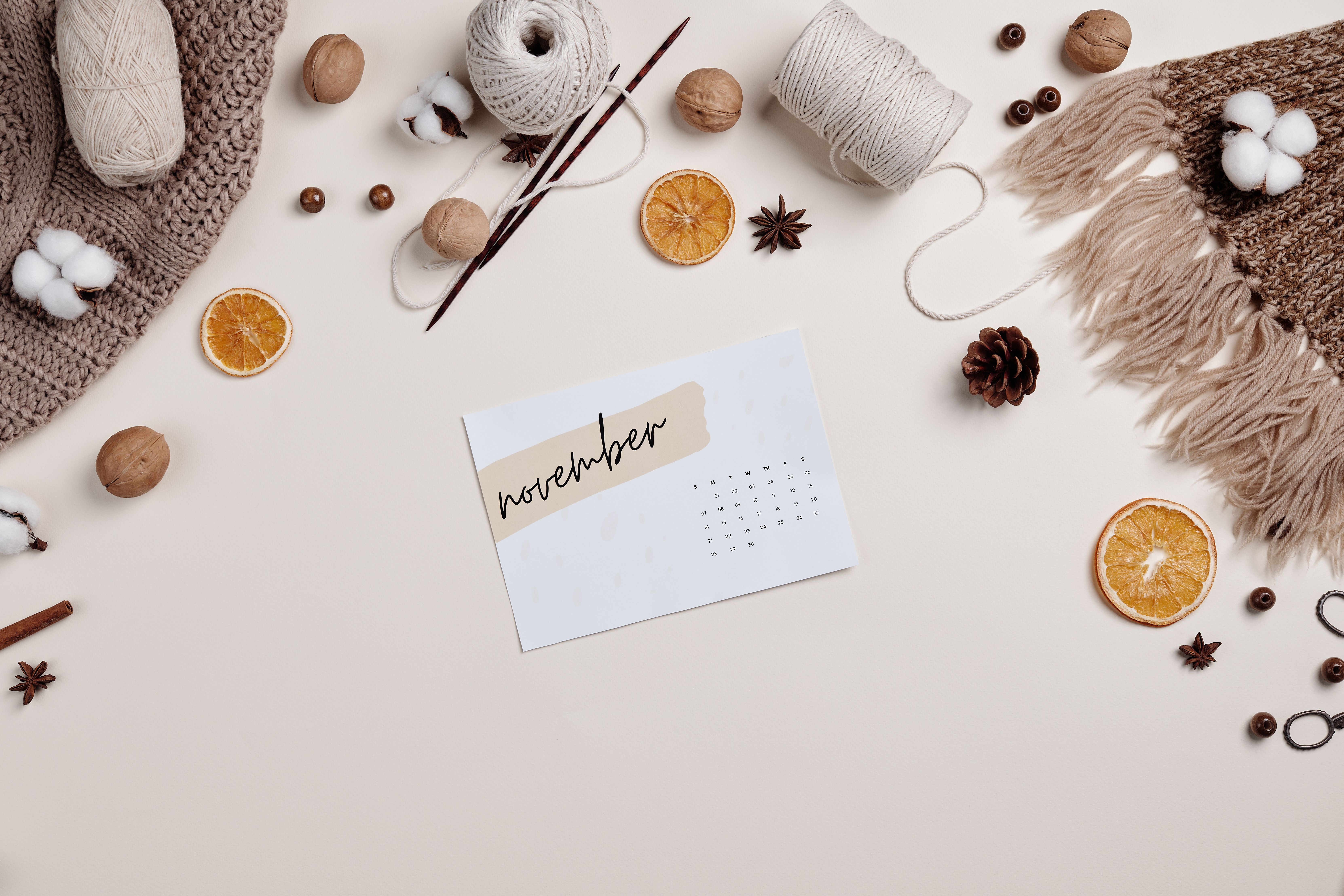 Flat lay of a cozy autumn setup with a November calendar, yarn, and dried oranges.
