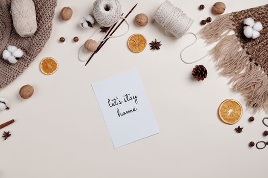 Flatlay of knitting materials, orange slices, and cozy decor with a 'Let's Stay Home' note.