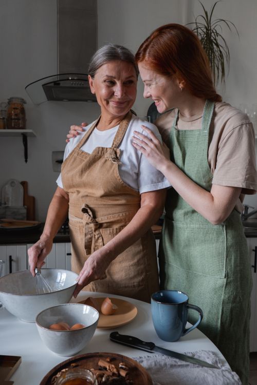 Free A mother and daughter smiling while preparing food in a cozy kitchen setting. Stock Photo