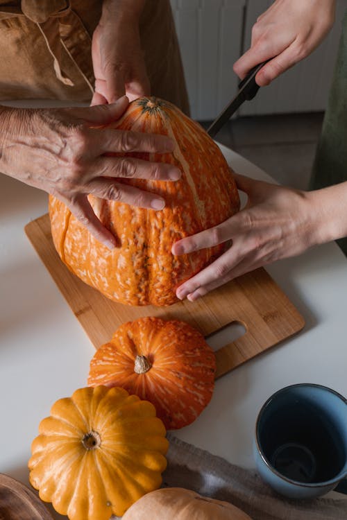 Person Holding Orange Pumpkin on Brown Wooden Chopping Board