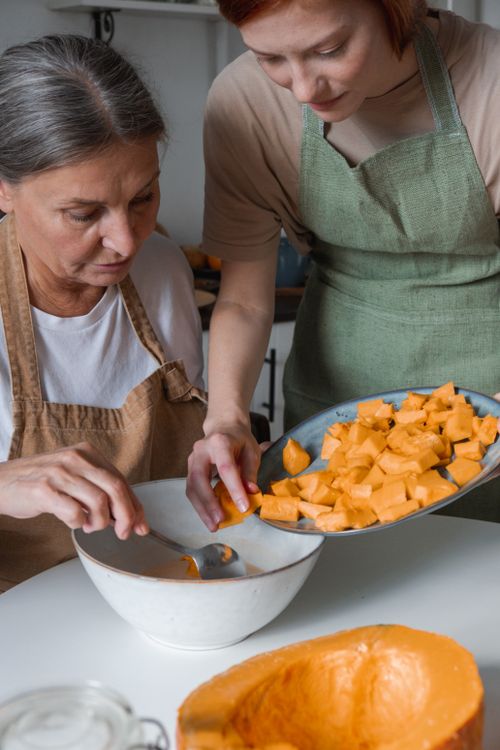 Free Mother and daughter cooking together, preparing squash for a meal in a cozy kitchen. Stock Photo