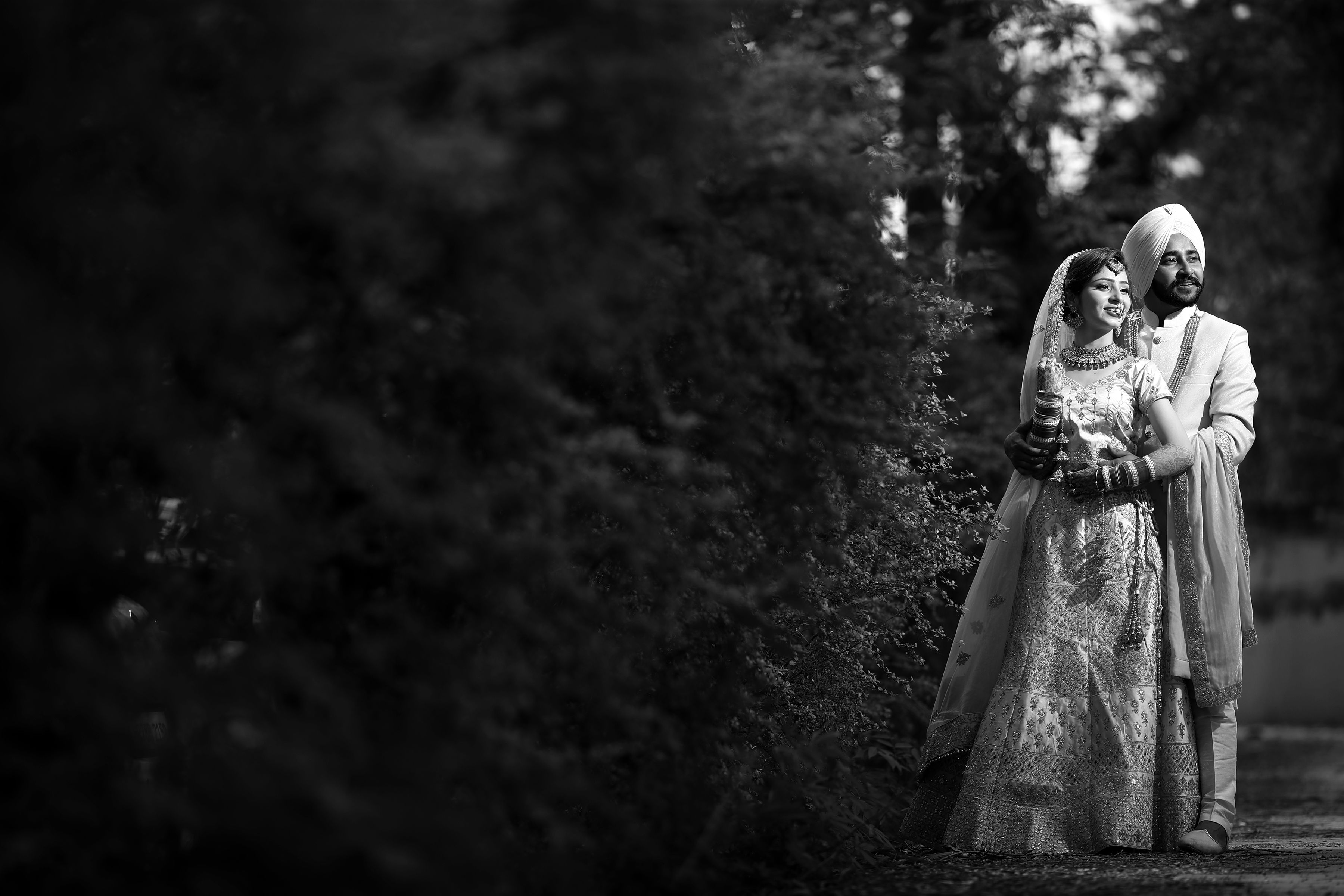 A couple in traditional Sikh attire embracing in a scenic outdoor setting.