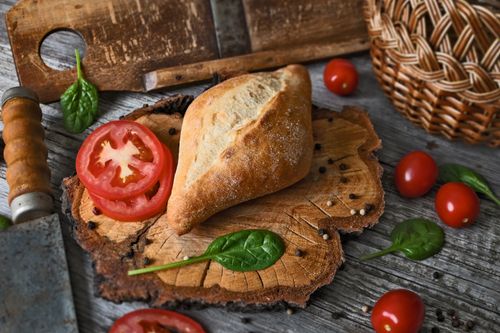 Free Freshly baked bread with sliced tomatoes and spinach leaves on a rustic wooden board. Stock Photo
