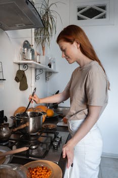 Woman stirring food in a pot on a stove in a modern kitchen setting.
