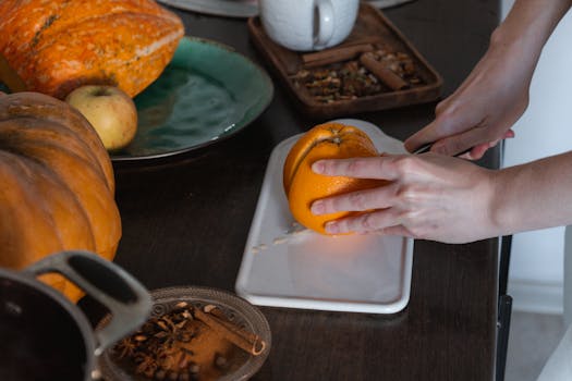 Close-up of hands slicing an orange with pumpkins and spices on a table.
