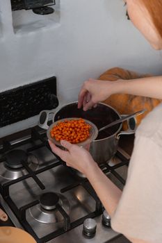 A woman cooking with orange berries in a kitchen, adding ingredients to a pot on a stove.