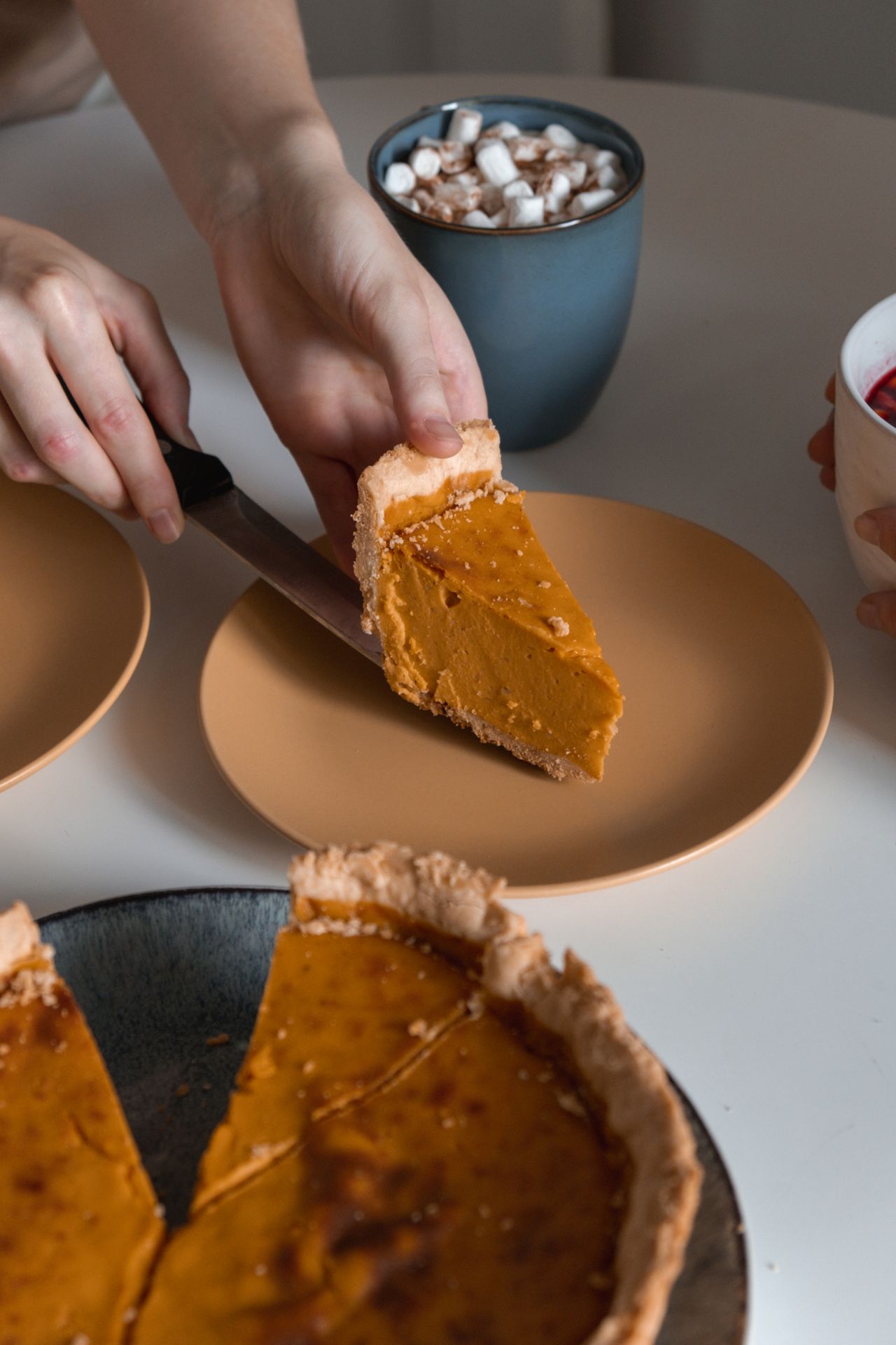 A hand lifting a slice of pumpkin pie from the pan with a server