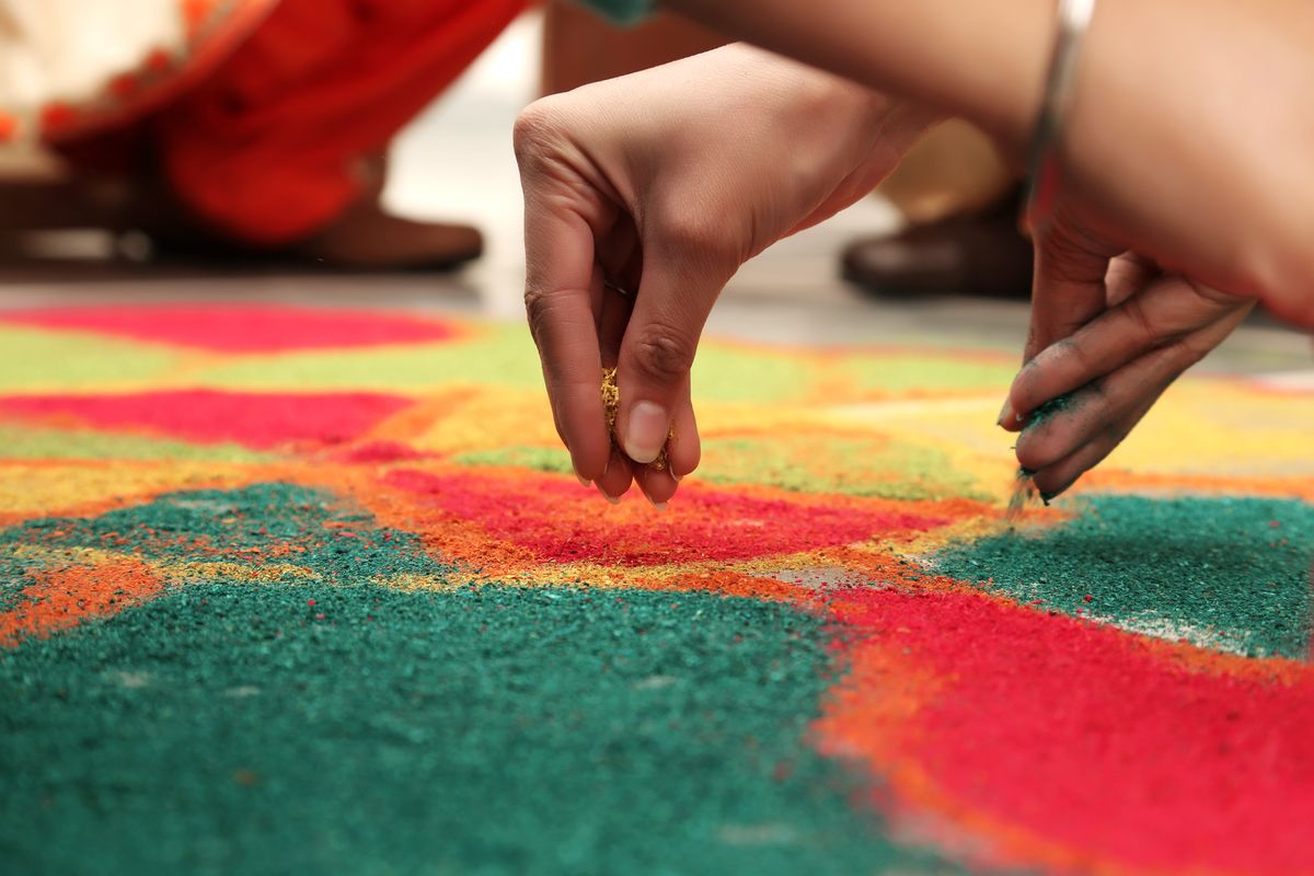 Hands creating a colorful mandala-style rangoli pattern with colored powder