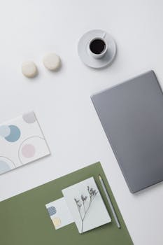 Flat lay of a clean desk with laptop, coffee, macaroons, and stationery in a minimalist style.