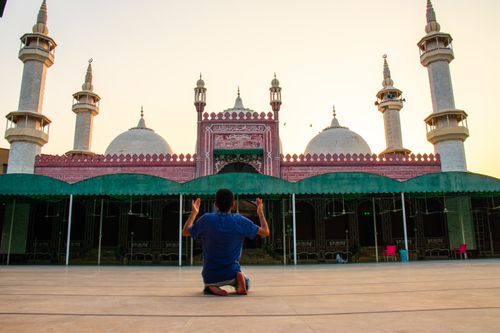 Free A man kneels in prayer outside a mosque in Faisalabad during sunset, showcasing Islamic architecture. Stock Photo