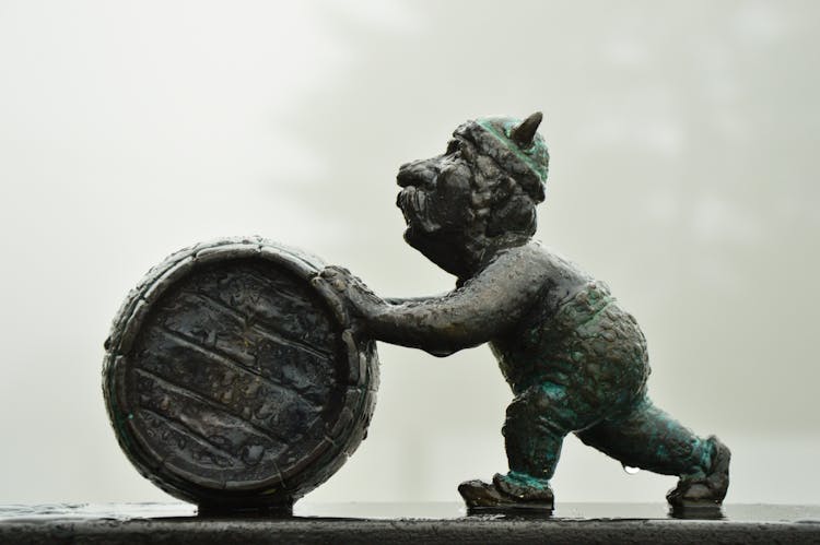 Figurine Of Elderly Man Pushing A Barrel 