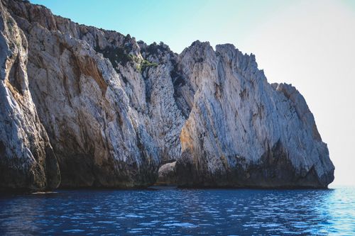 Free Range of tall steep beige mountains with bushes on top on shore of ocean under light blue cloudless sky Stock Photo