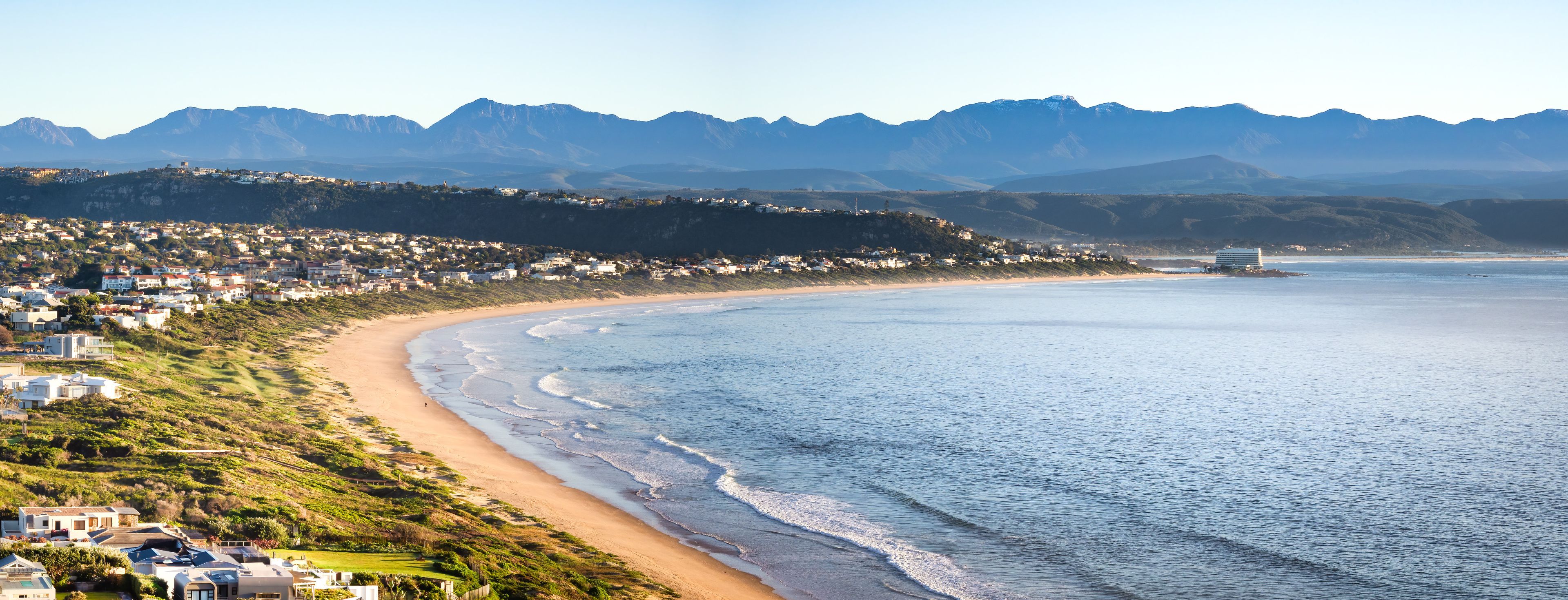 Breathtaking aerial view of Plettenberg Bay's coastline with mountains and seaside homes.