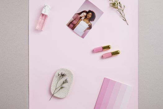 Elegant flat lay with cosmetics, photo, and pastel elements on a pink background.