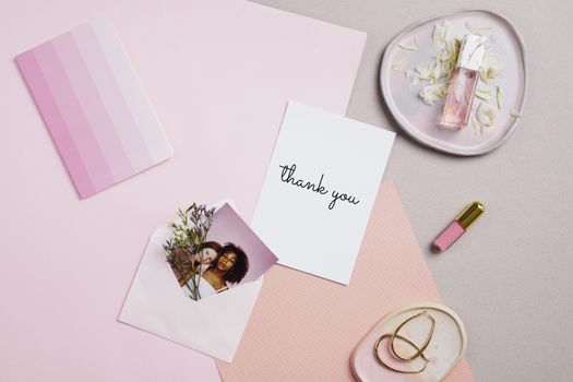 Flatlay of a thank you card with pink-themed accessories, including perfume and earrings.