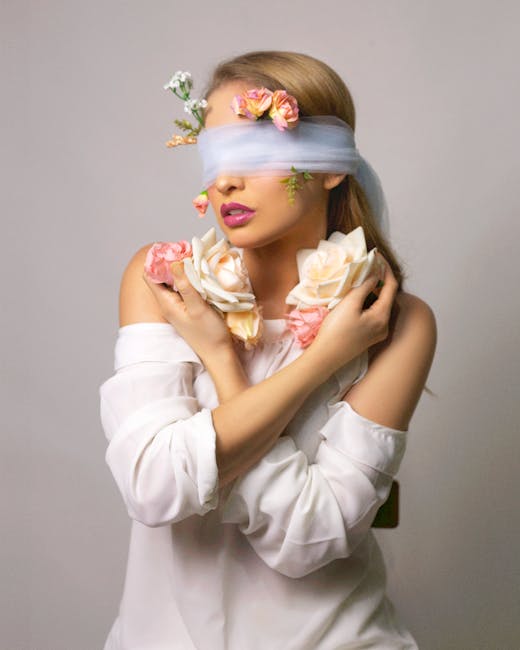 Eccentric emotionless young female hiding eyes in bandage with roses on gray background