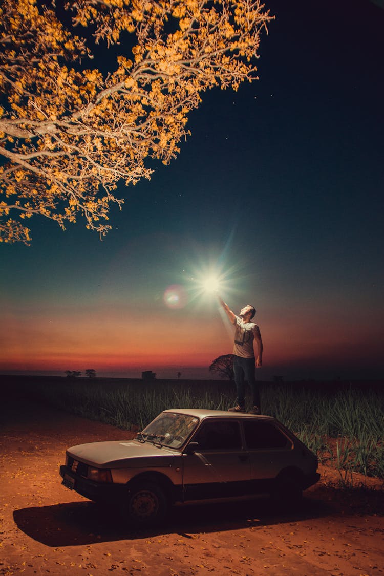 A Man Standing On Top Of The Car Parked On The Street At Night