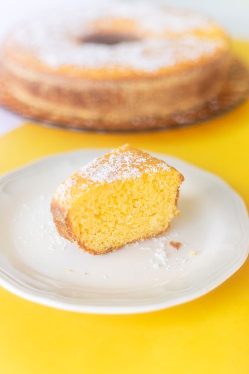Free Appetizing homemade piece of cake served on white plate on yellow table with whole cake on blurred background in kitchen Stock Photo