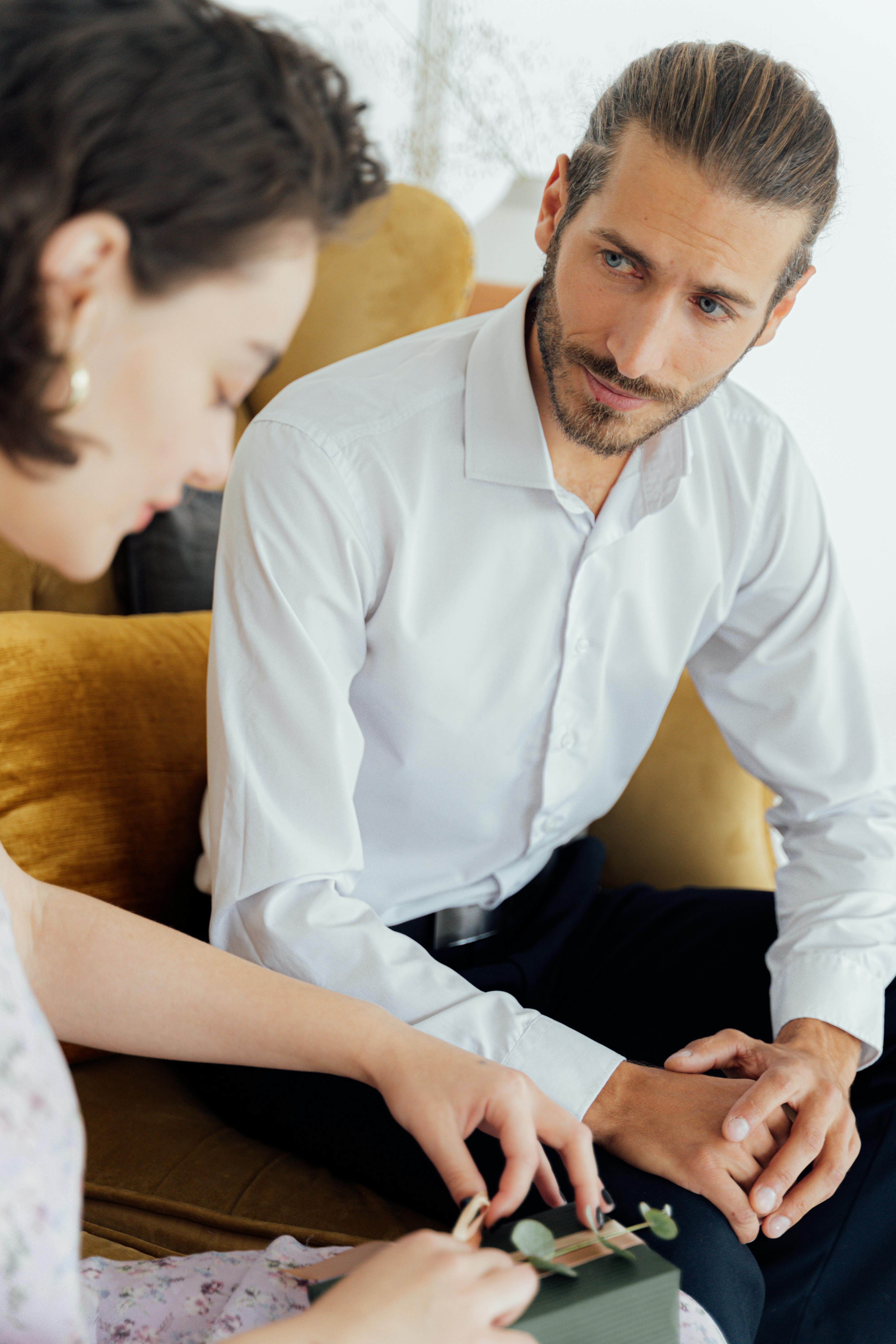 A couple seated indoors engaging in a heartfelt moment of gift giving and connection.