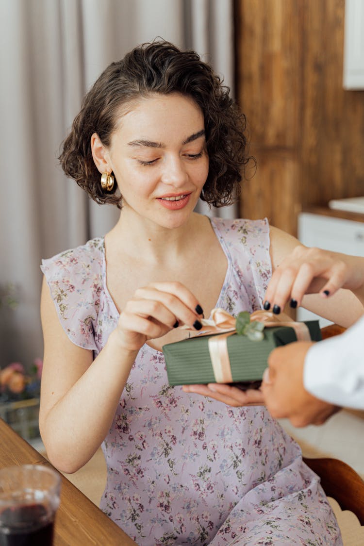 A Woman In A Floral Dress Opening A Present