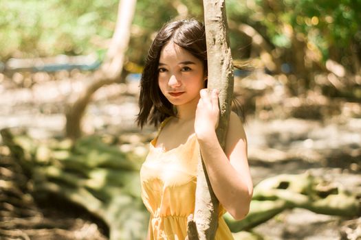 一位富有洞察力的年轻少数族裔女性，黑发垂落，手扶细长的树干，在模糊的日光背景下注视着相机