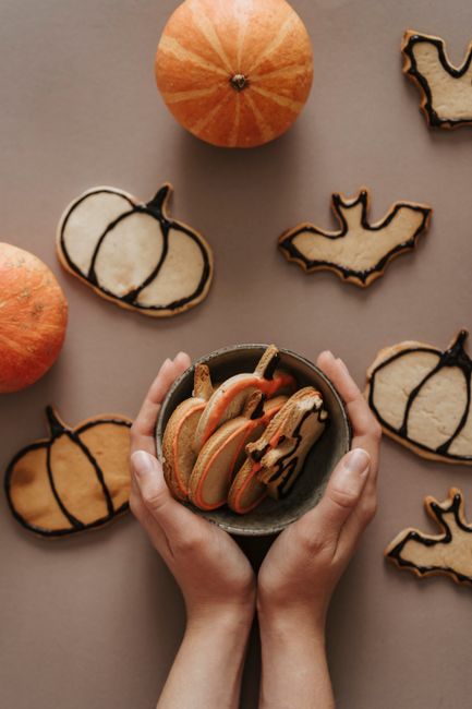 A cooling rack of cut-out sugar cookies shaped like bats, pumpkins, and ghosts, iced in orange and black royal icing with piped details.