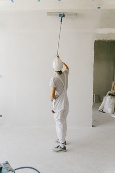 一位画家穿着工作服、戴着安全帽，正用滚筒粉刷内墙，这是他的后视图