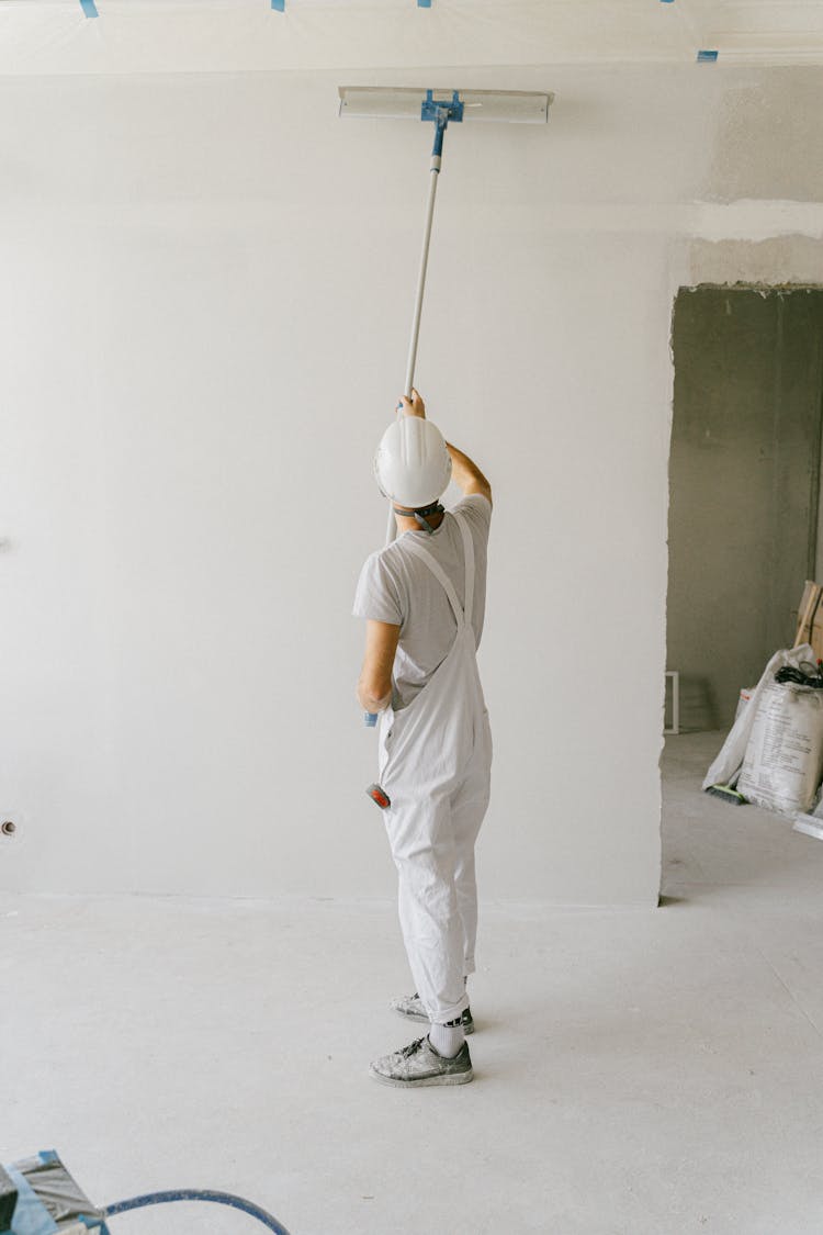 Back View Of A Person Painting The Wall Using A Painting Brush Roller