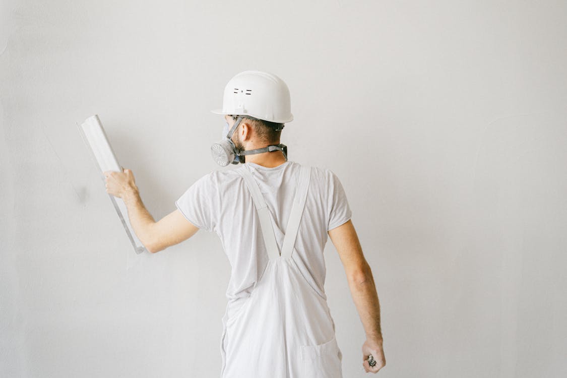 Free Back view of a construction worker in safety gear plastering a white wall. Stock Photo