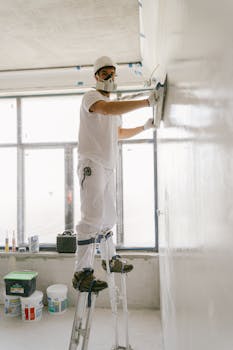 Construction worker smoothing a wall indoors using safety gear.