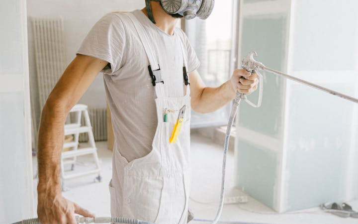 A construction worker wearing a gas mask and holding a hose in a renovation site.