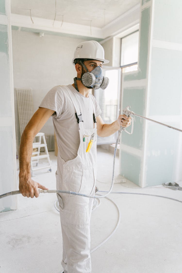 A Man Wearing Gas Mask And Hard Hat Using A Hose