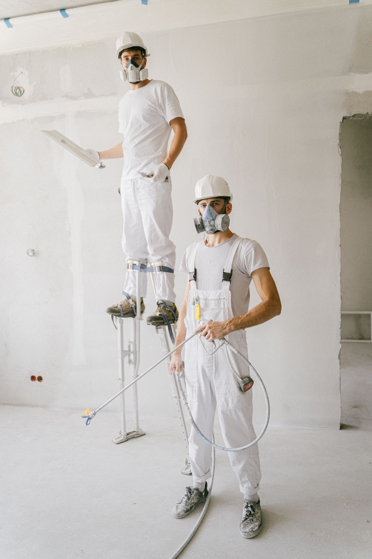Painter in white overalls and a respirator mask working on a prepared interior wall
