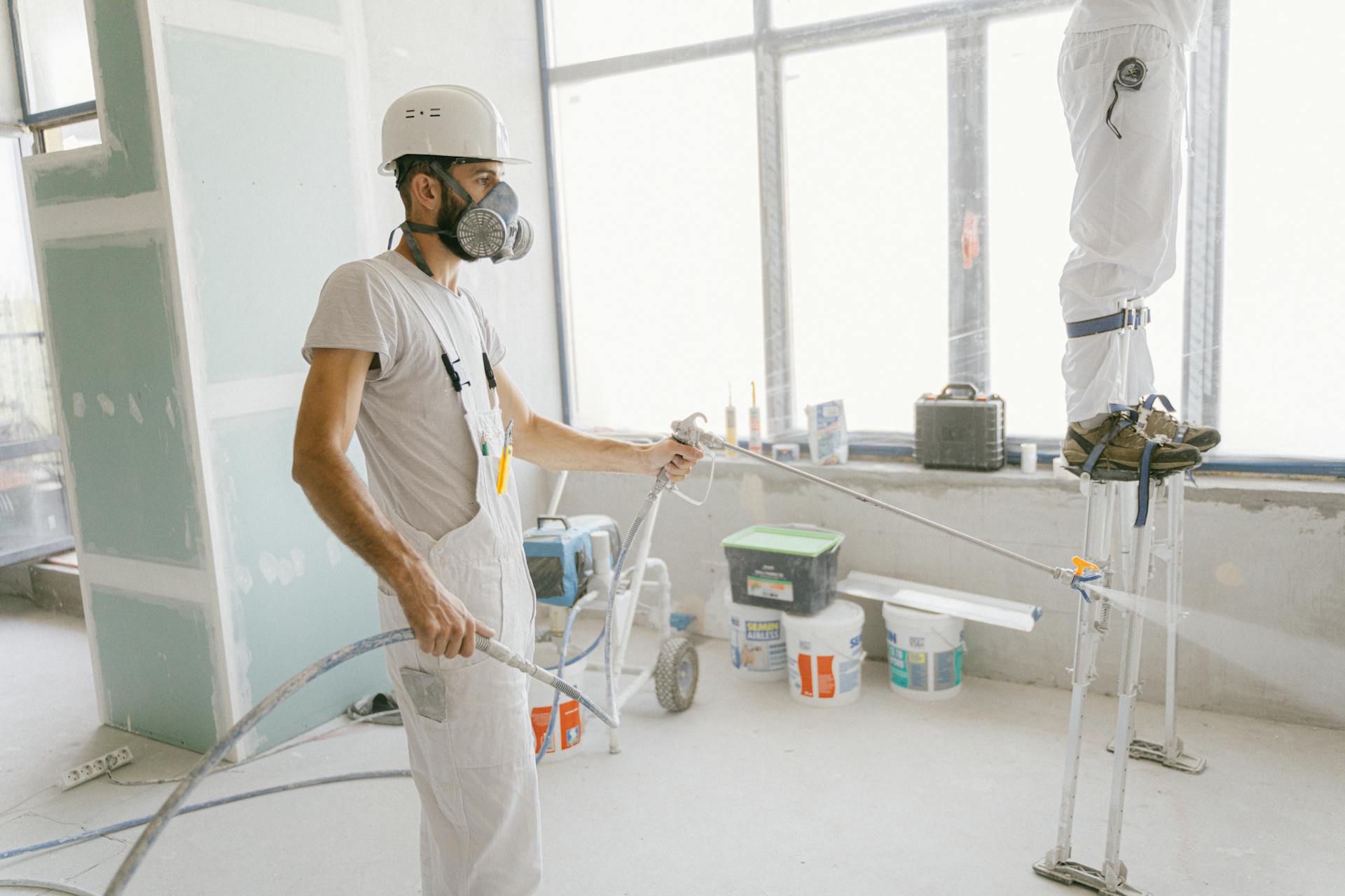 Man in White T-shirt Wearing Hard Hat Using a Hose to Wash the House