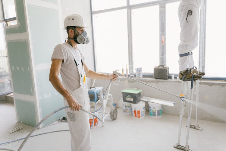 Man In White T-shirt Wearing Hard Hat Using A Hose To Wash The House