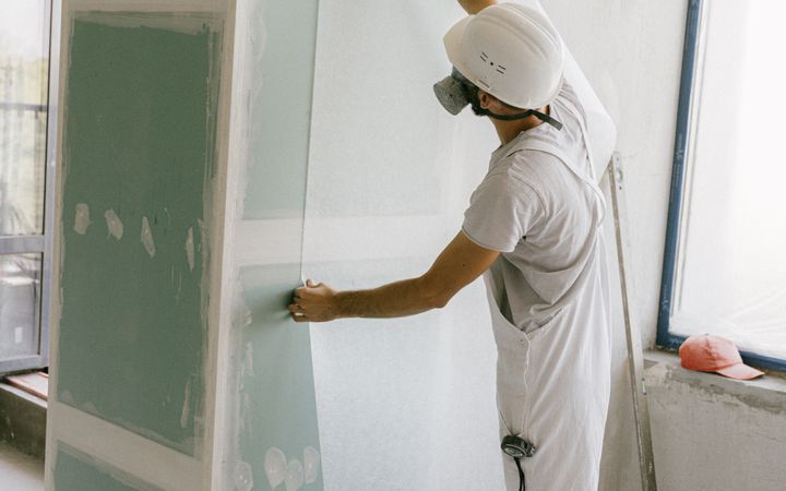 Construction worker in hard hat applying wallpaper inside a building under renovation.