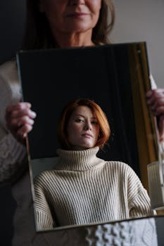 镜中映照出一位身穿针织衫的红发女子，营造出沉思的氛围