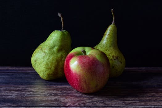 A classic still life composition featuring an apple and two pears on a wooden table, perfect for culinary and artistic themes.
