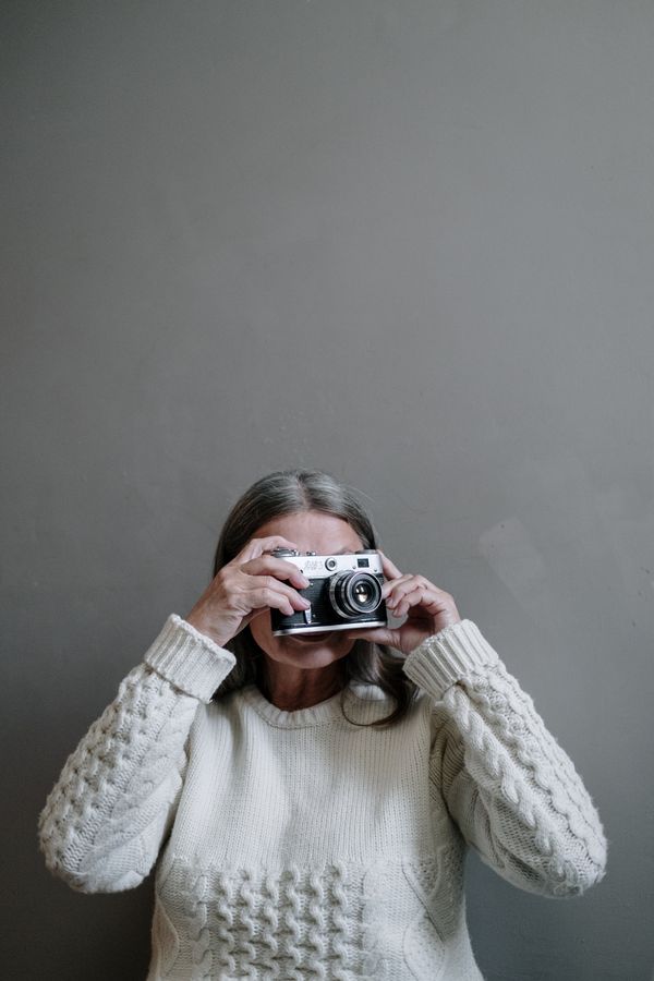 An older woman in a knitted sweater taking a photograph with a vintage camera