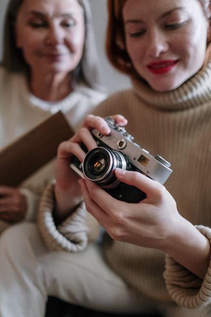 Two women examining a vintage camera while sitting indoors. Cozy and vintage atmosphere.