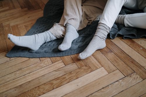 Free A couple wearing socks, relaxing on a wooden floor with a gray blanket, enjoying warmth. Stock Photo