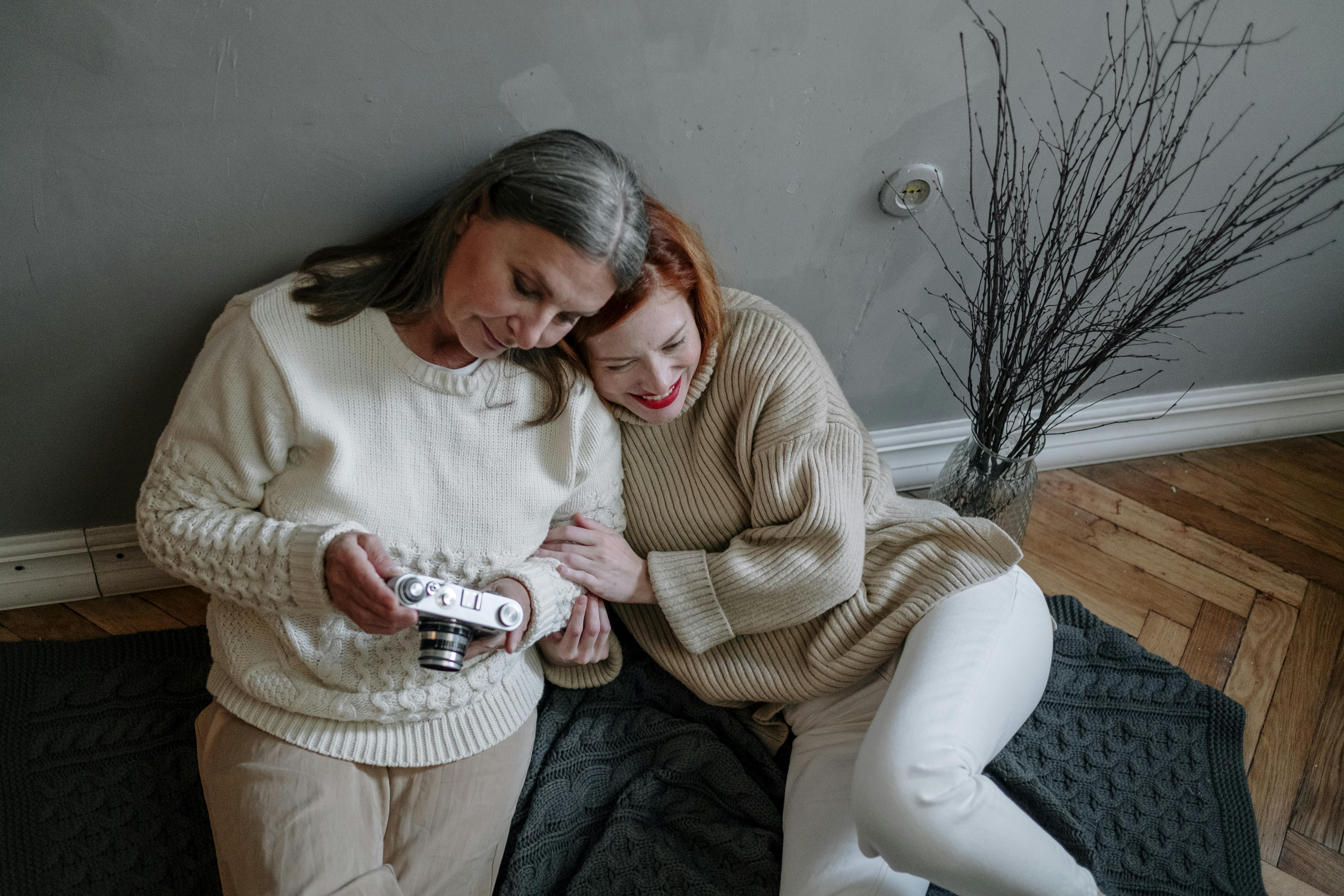 two women leaning on gray wall