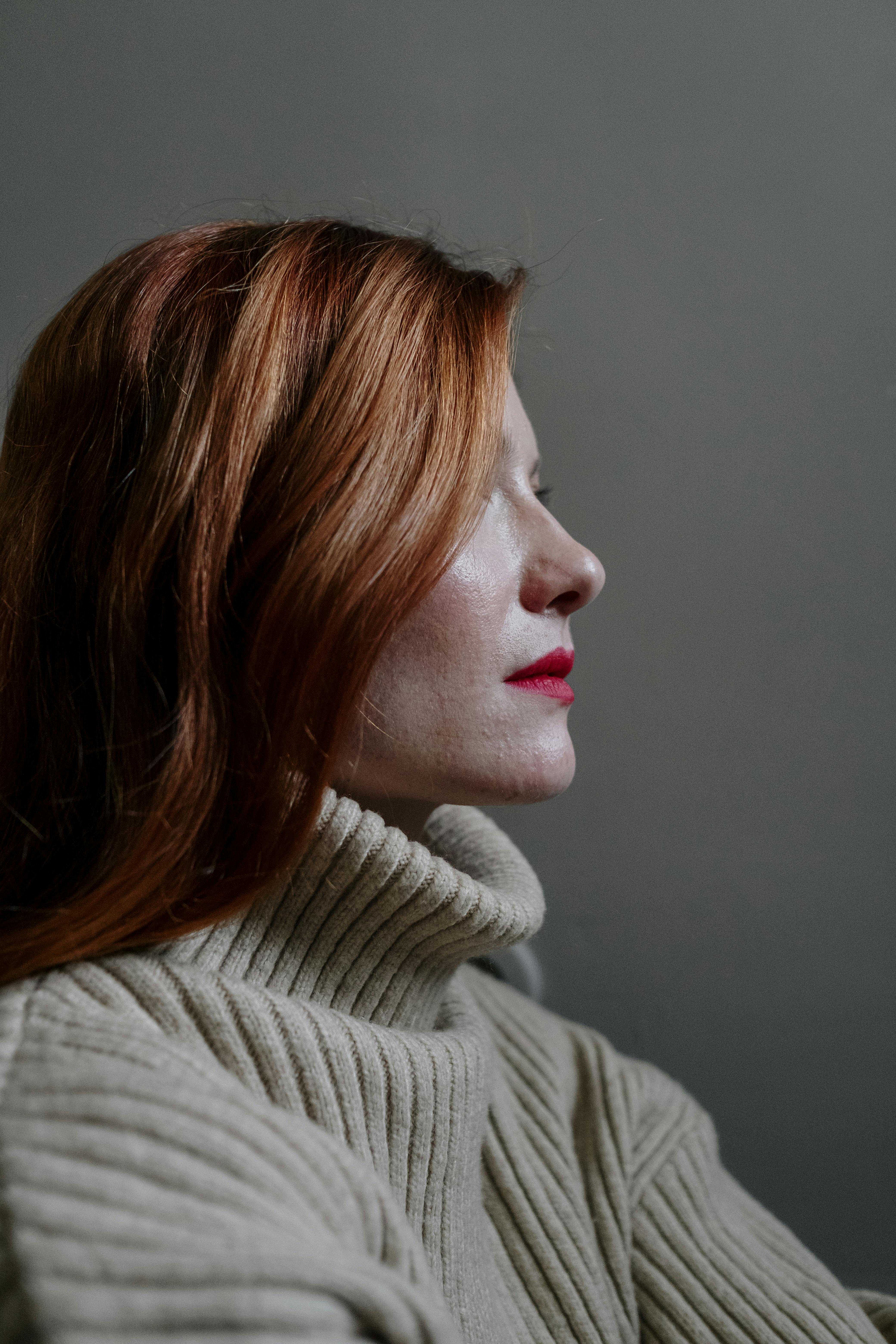 Side view of a red-haired woman in a knitted sweater against a gray background.