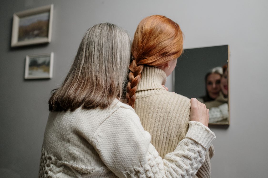 Free A touching moment of a mother and daughter in knitted sweaters reflected in a mirror. Stock Photo