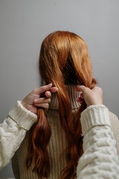 一名女子在室内灰色背景下，用针织毛衣编织红色头发的详细特写